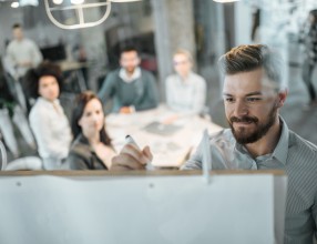 Mann schreibt vor einem Team mit vier Personen etwas an ein Whiteboard